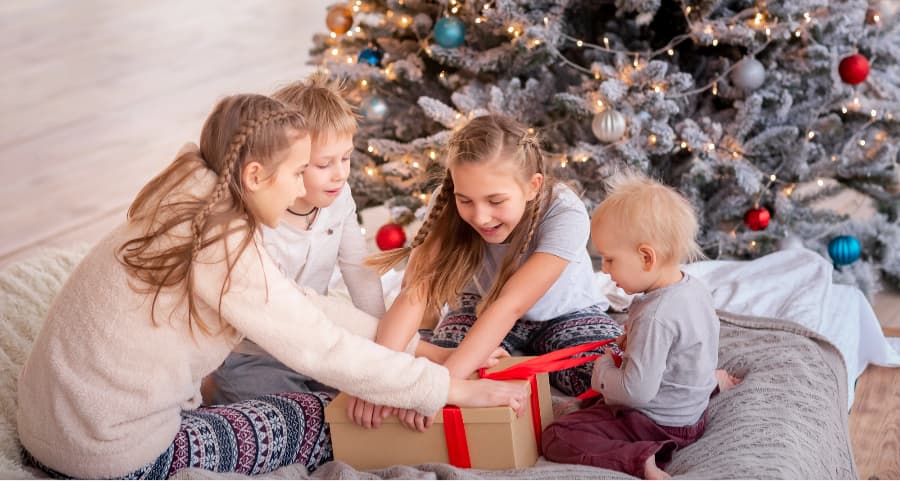 Children opening a present in the family room near a Christmas tree.